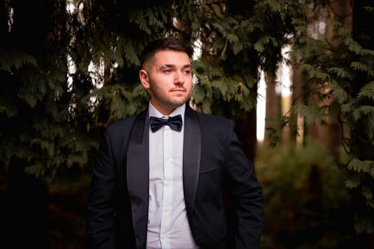 A young man in a tuxedo poses in a forest setting, displaying elegance and sophistication.