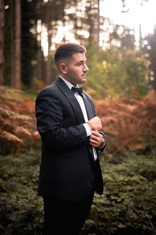 Free A man in a formal black suit stands thoughtfully in a lush outdoor setting with fall foliage. Stock Photo