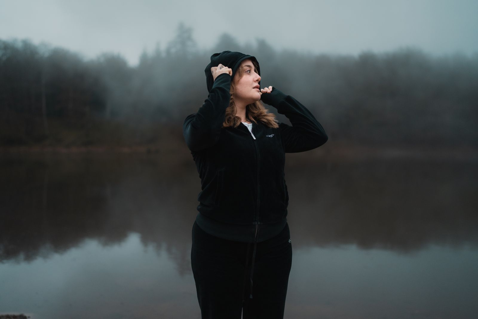 Figure in a hooded shell standing at a misty lake — photo by Andrea Prochilo on Pexels