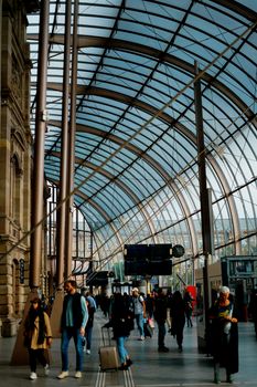 Travelers walking under a modern glass ceiling in a busy train station, showcasing urban transit life.