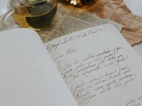 A beautifully handwritten letter on open notebook next to a cup of tea on textured paper background.