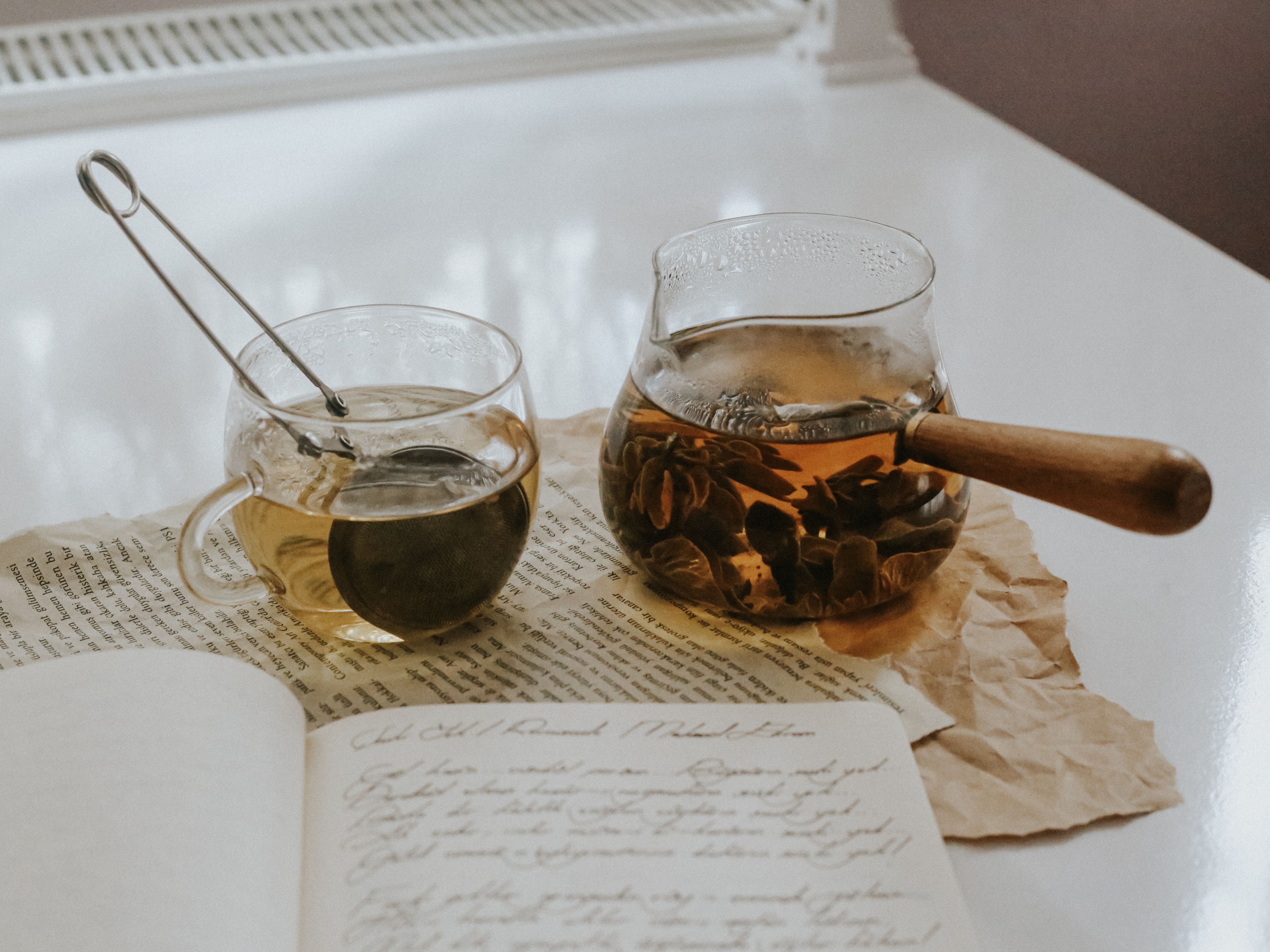 A wooden tea flight board with three small glass cups of different brews and handwritten tasting notes on kraft paper tags.