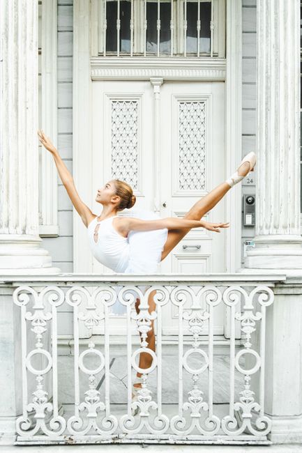A ballet dancer in a white outfit performs a graceful pose on an ornate balcony in Istanbul, Türkiye.