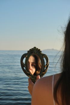 A woman's reflection in an ornate mirror by the sea at sunset in Istanbul, Türkiye.