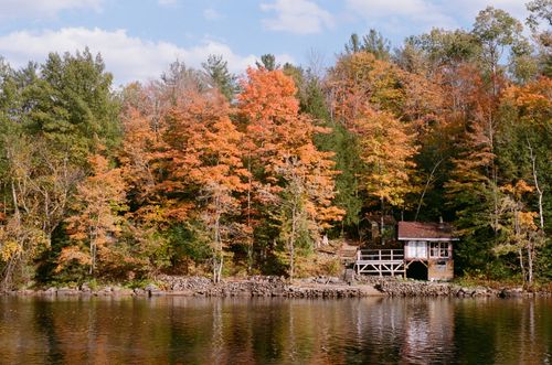 Free Charming lakeside cabin amidst colorful fall foliage, serene and inviting. Stock Photo