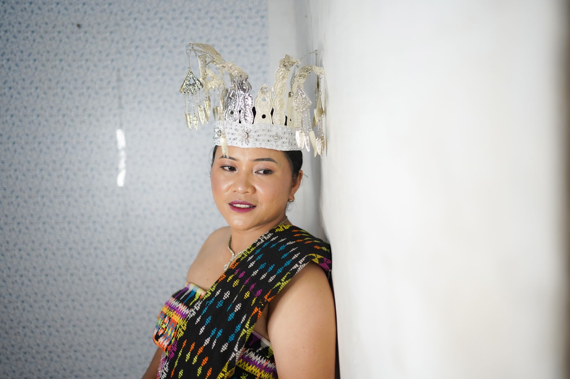 Woman in traditional Timorese attire featuring an ornate headpiece, captured indoors with bright lighting.