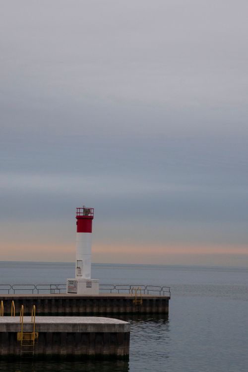 Free A tranquil scene of a lighthouse standing on a pier beside calm waters during dusk. Stock Photo