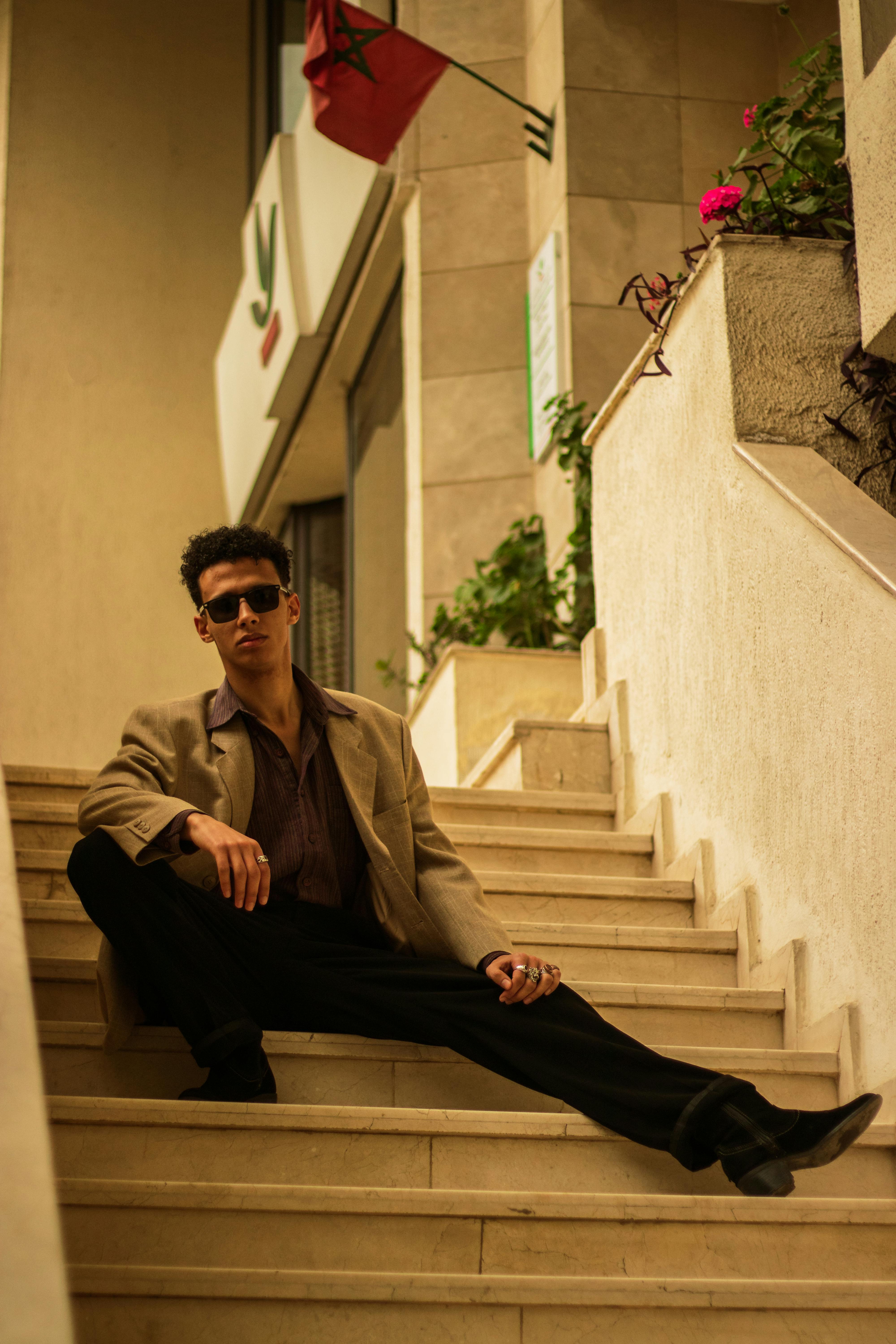 A fashionable man in sunglasses sitting on stairs in Meknes, Morocco. Urban chic style.