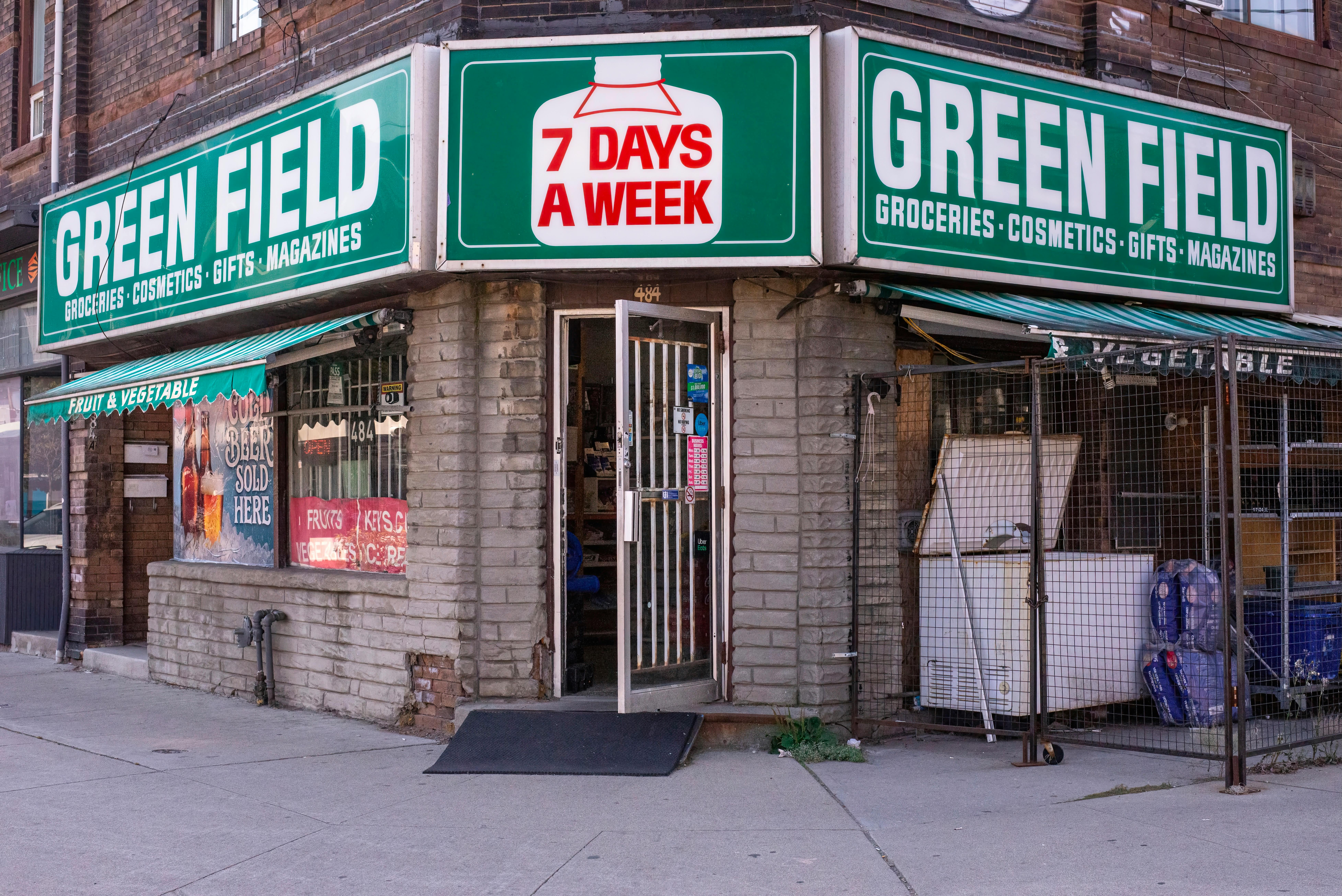 A vibrant local grocery store entrance with fresh produce spilling onto the sidewalk, locals shopping