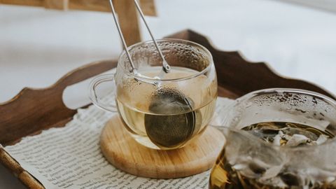 A warm, cozy scene showcasing glass teacups with tea infuser on a tray with scattered papers.