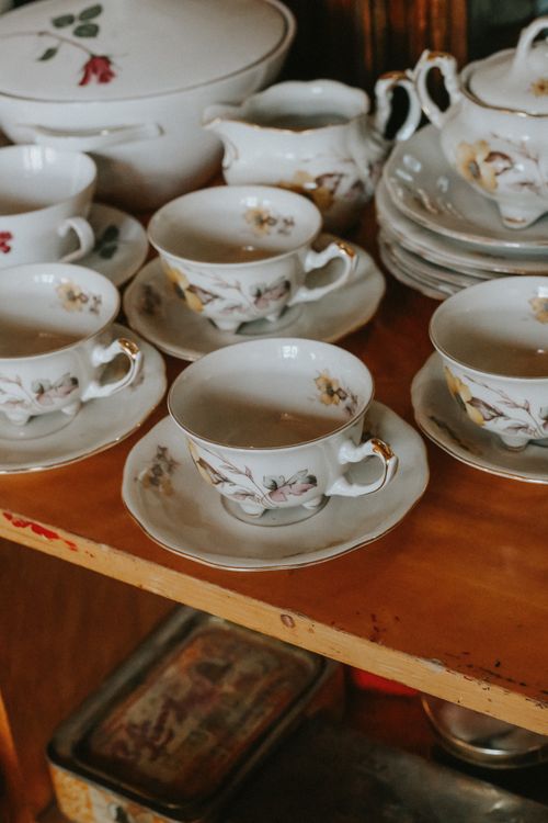 Free A collection of vintage porcelain tea cups and saucers with floral designs on a wooden shelf. Stock Photo