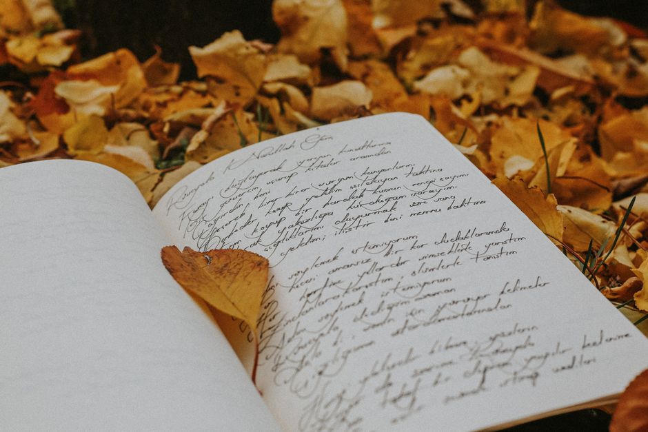An open notebook with handwritten calligraphy surrounded by fall leaves, evoking a cozy and reflective autumn atmosphere.