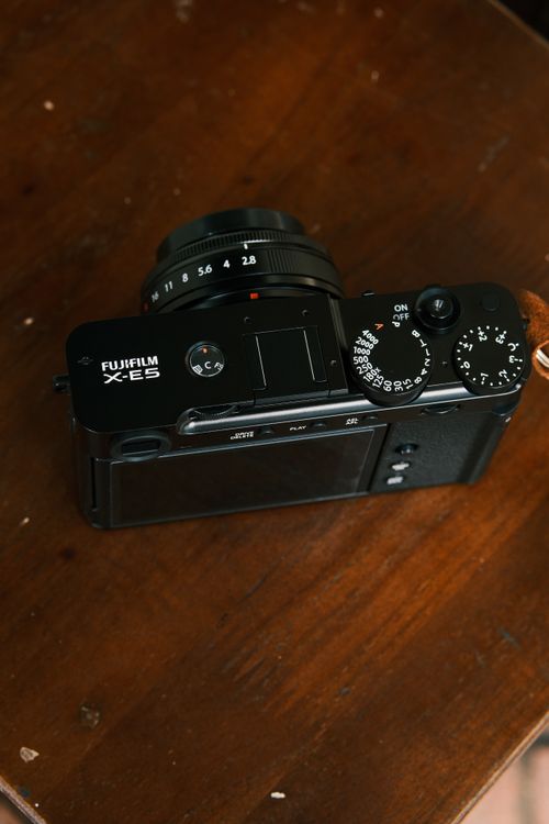 Free A Fujifilm X-E5 camera resting on a wooden surface, showcasing its controls. Stock Photo