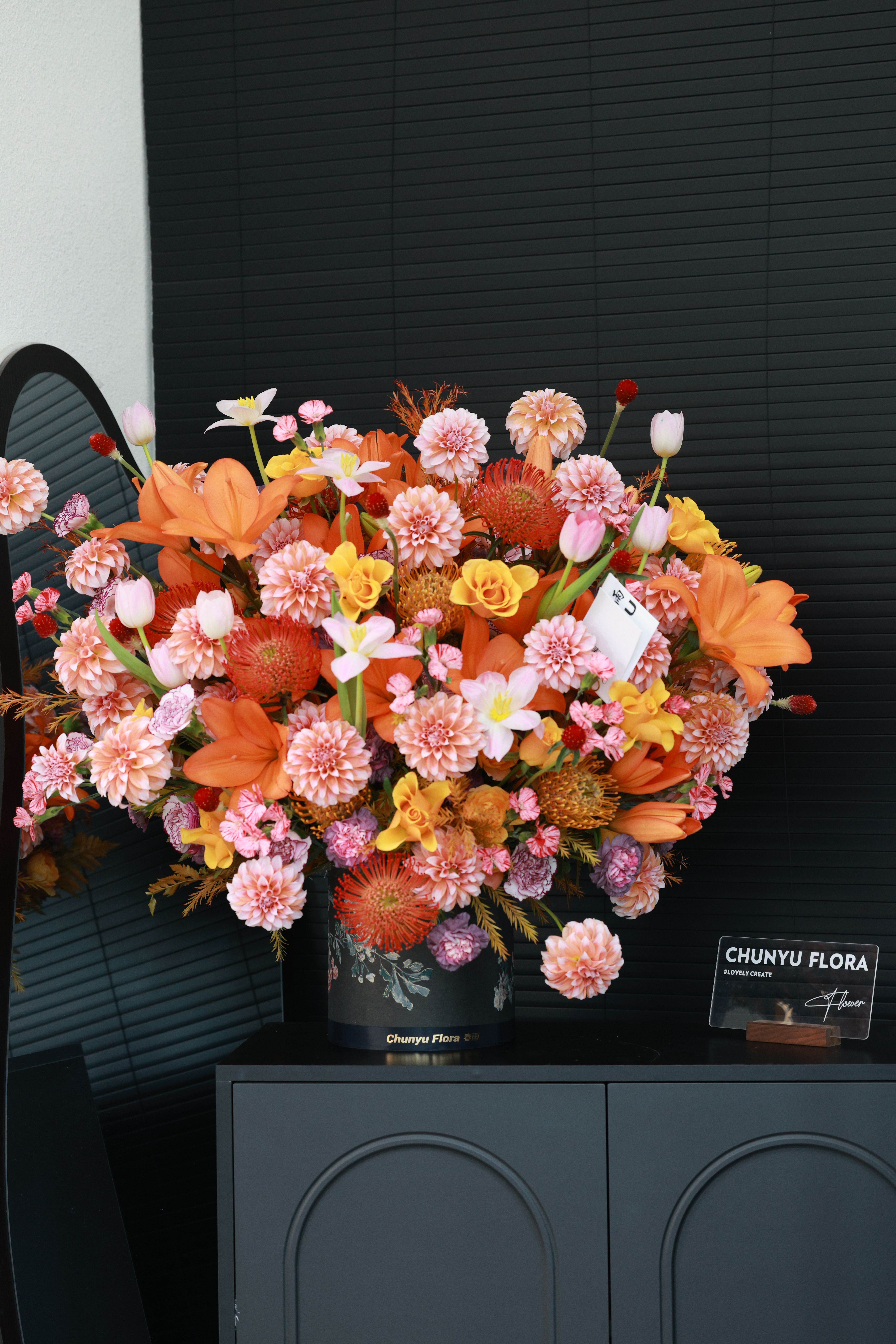 Colorful flower arrangement with orange and pink blooms in a black vase indoors.
