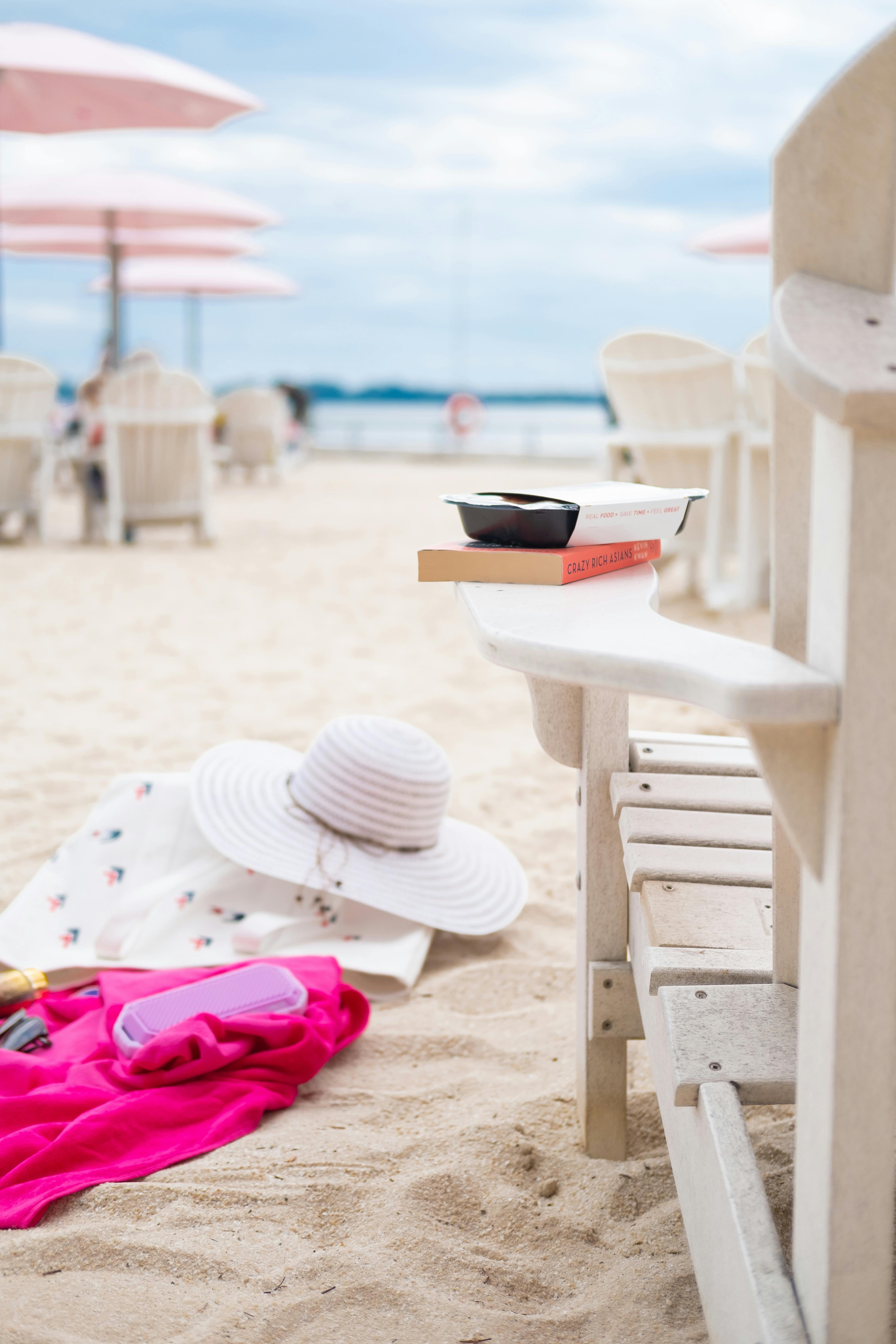 Free A serene beach scene with an armchair, sun hat, and book on a sandy shore, capturing summer vibes. Stock Photo