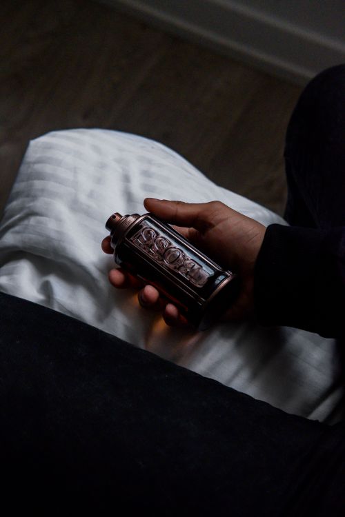 Free Artistic shot of a hand holding a dark-toned perfume bottle indoors, showcasing elegance and luxury. Stock Photo