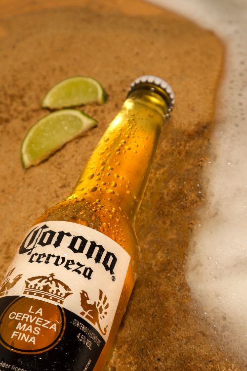 Free A chilled beer bottle on sandy beach with lime wedges, exuding refreshing summer vibes. Stock Photo