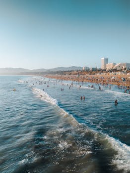 A bustling summer day at Santa Monica beach with people enjoying the ocean waves and sun. by Vinicius Maciel