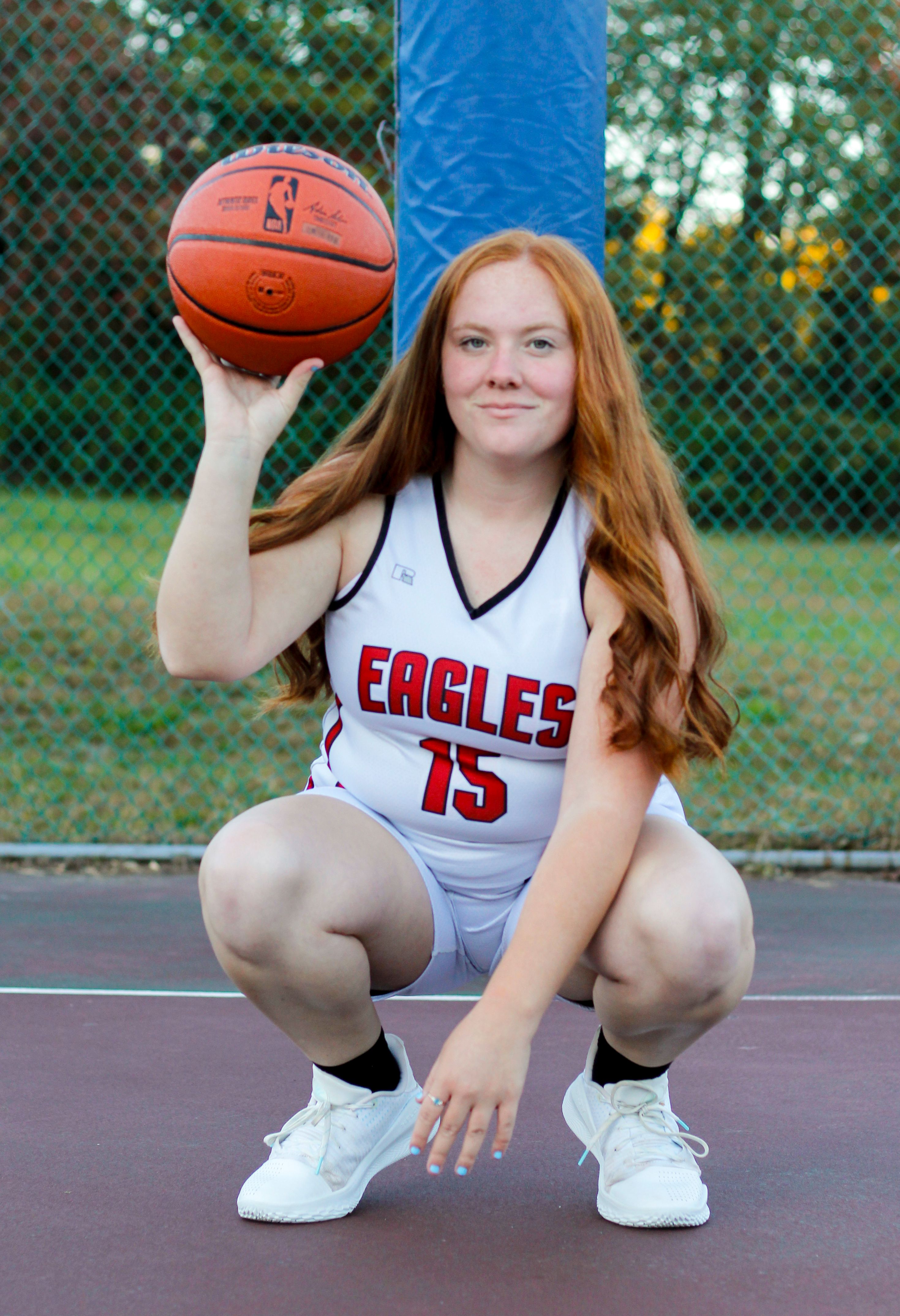 Young female basketball player posing on an outdoor court with a ball.