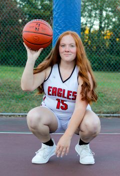 Young female basketball player posing on an outdoor court with a ball.