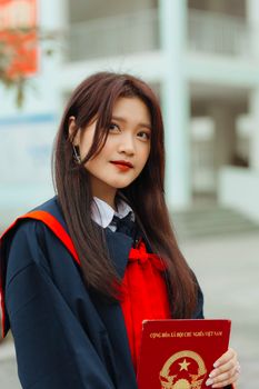 Portrait of a young female graduate holding a red diploma outdoors.