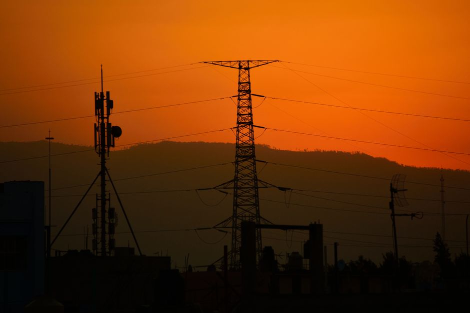 Power lines silhouetted against an orange sunset sky, conveying energy and tranquility.