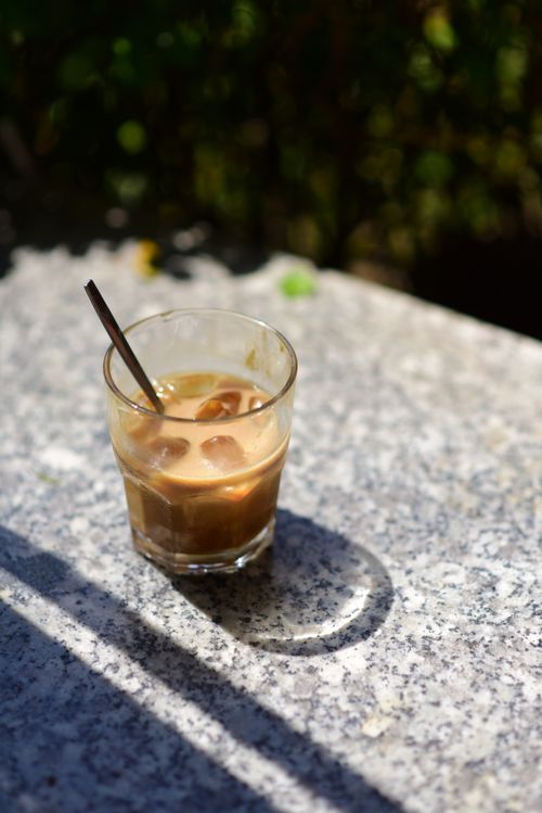 Free A single glass of iced coffee with a straw on a sunlit stone table outdoors. Stock Photo