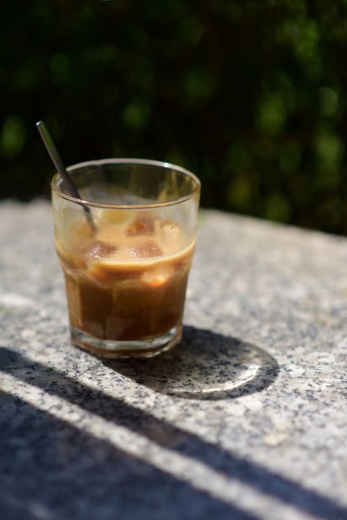 Free A glass of iced coffee with a straw on a sunlit outdoor table, creating a summer vibe. Stock Photo