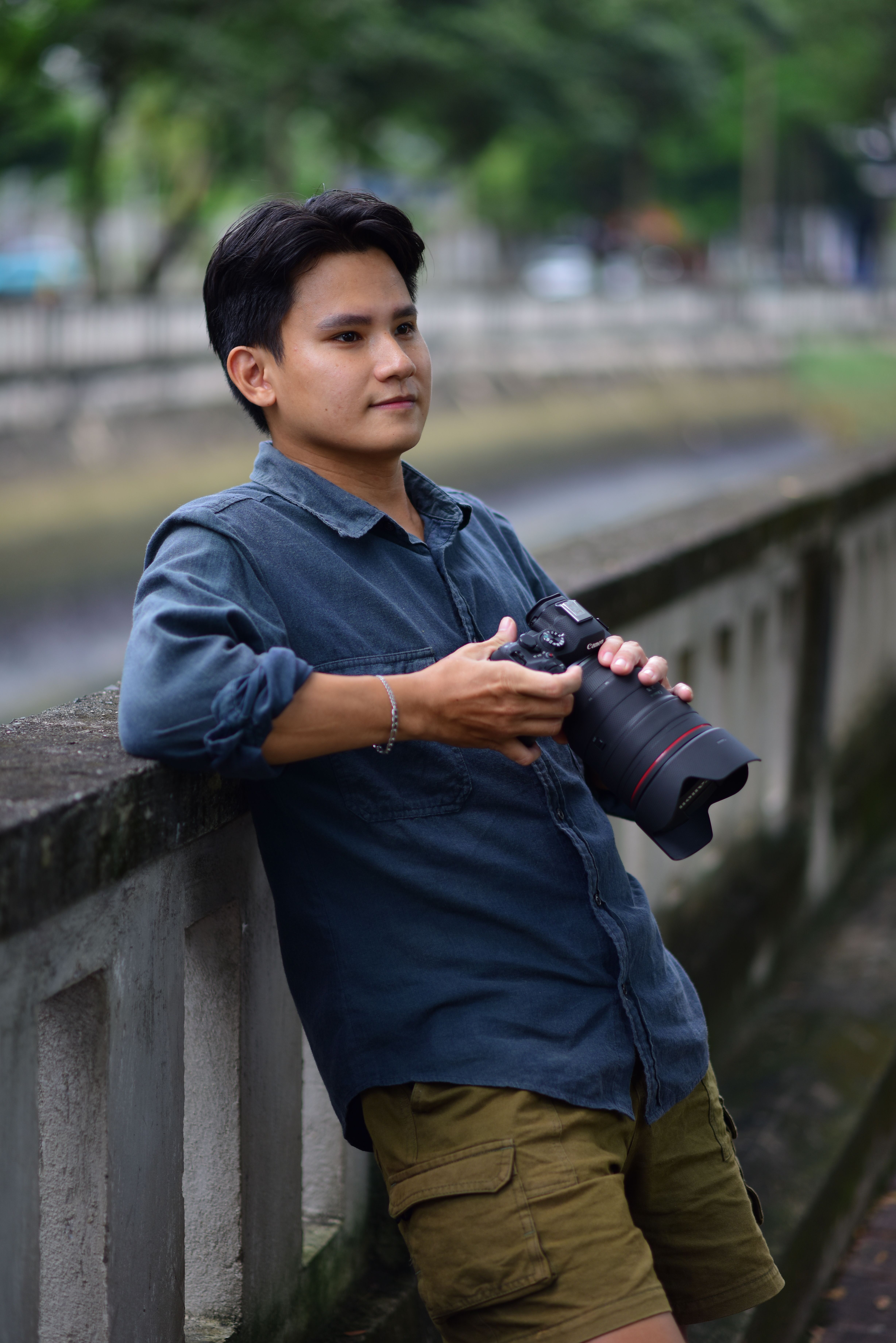 Young man with camera relaxing outdoors by concrete railing.