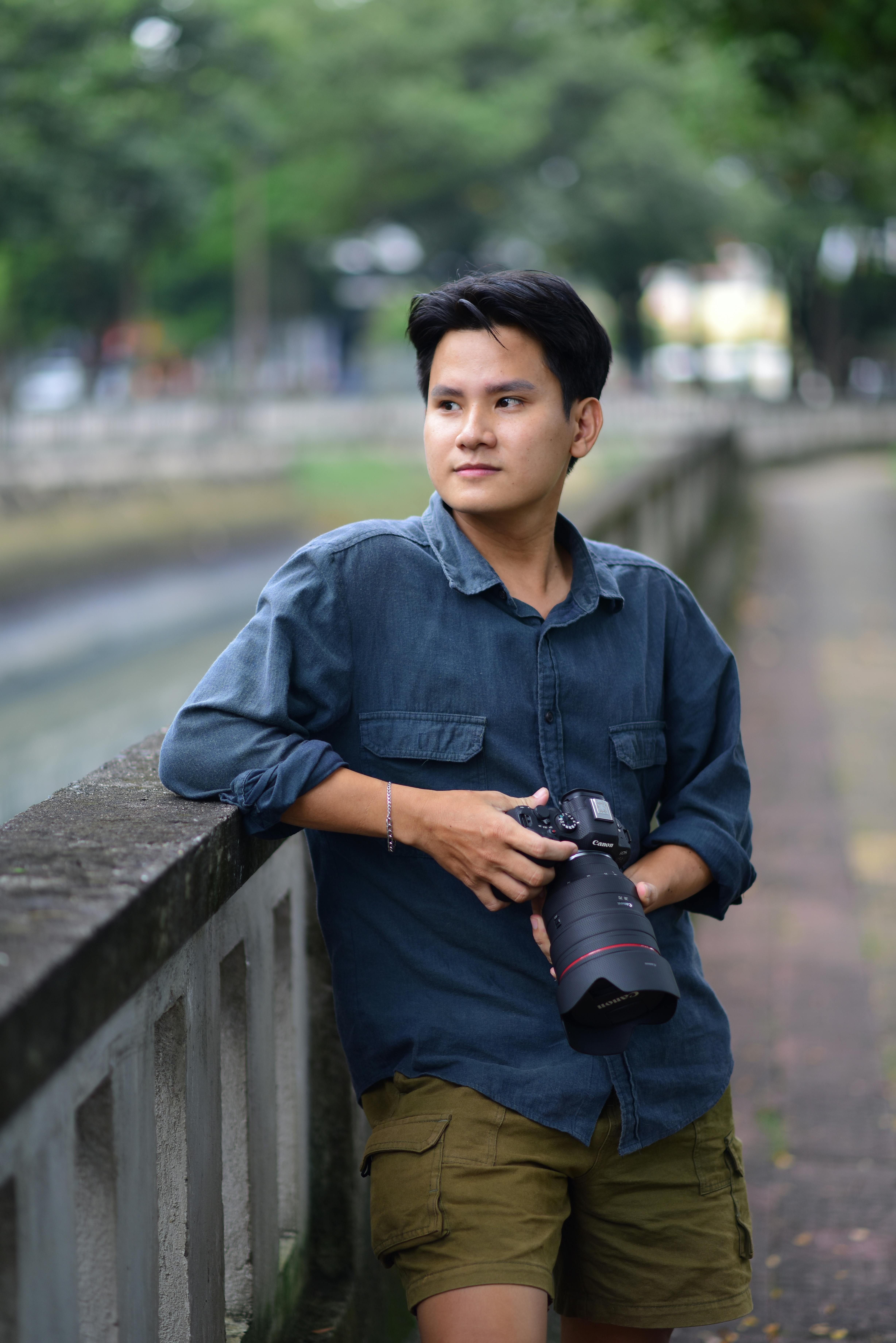 Portrait of a young man with a camera in a relaxed outdoor setting.