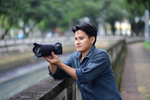 Free Man holding a camera outdoors, capturing urban scenery. Stock Photo