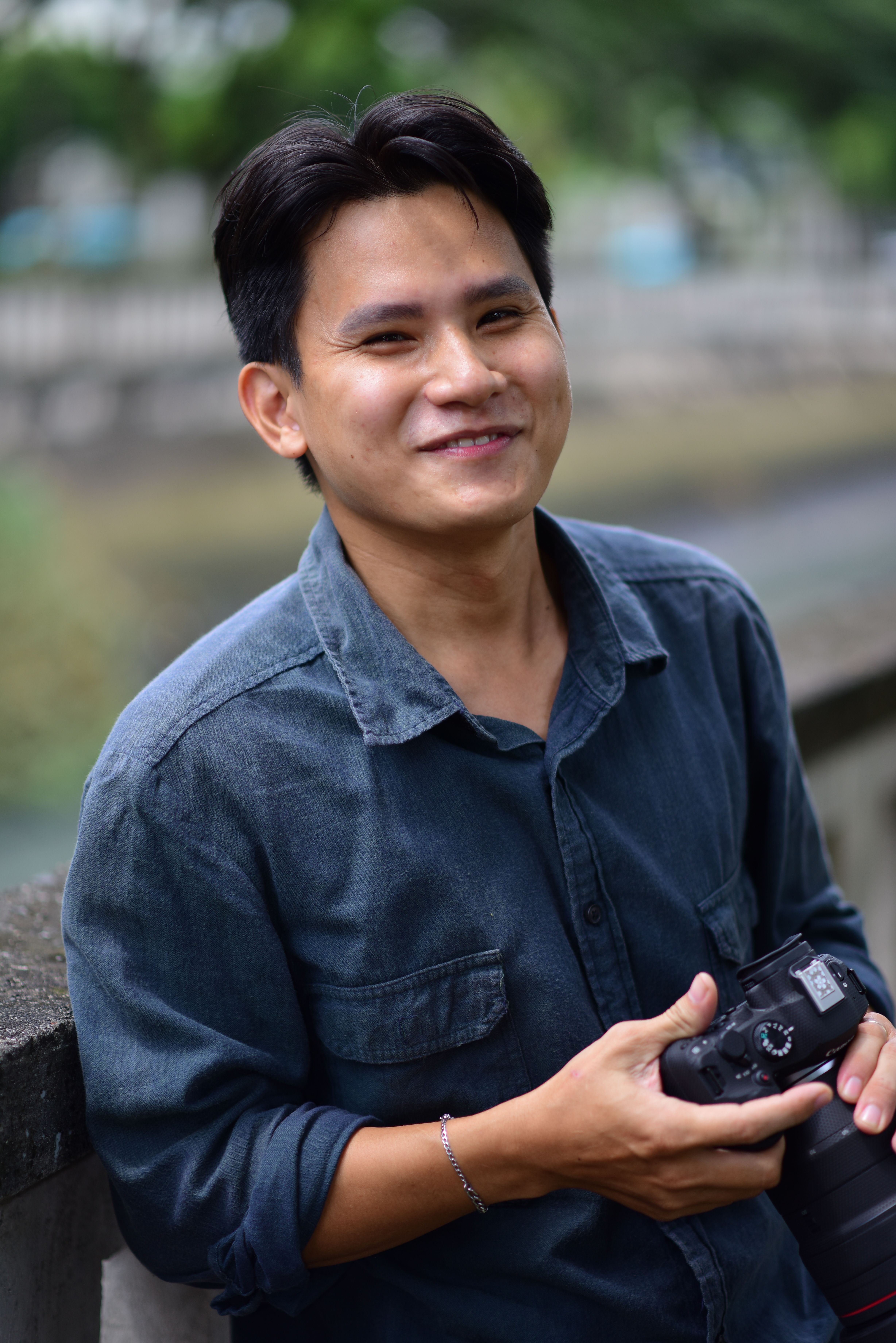Smiling photographer holding a camera outdoors, wearing a denim shirt.