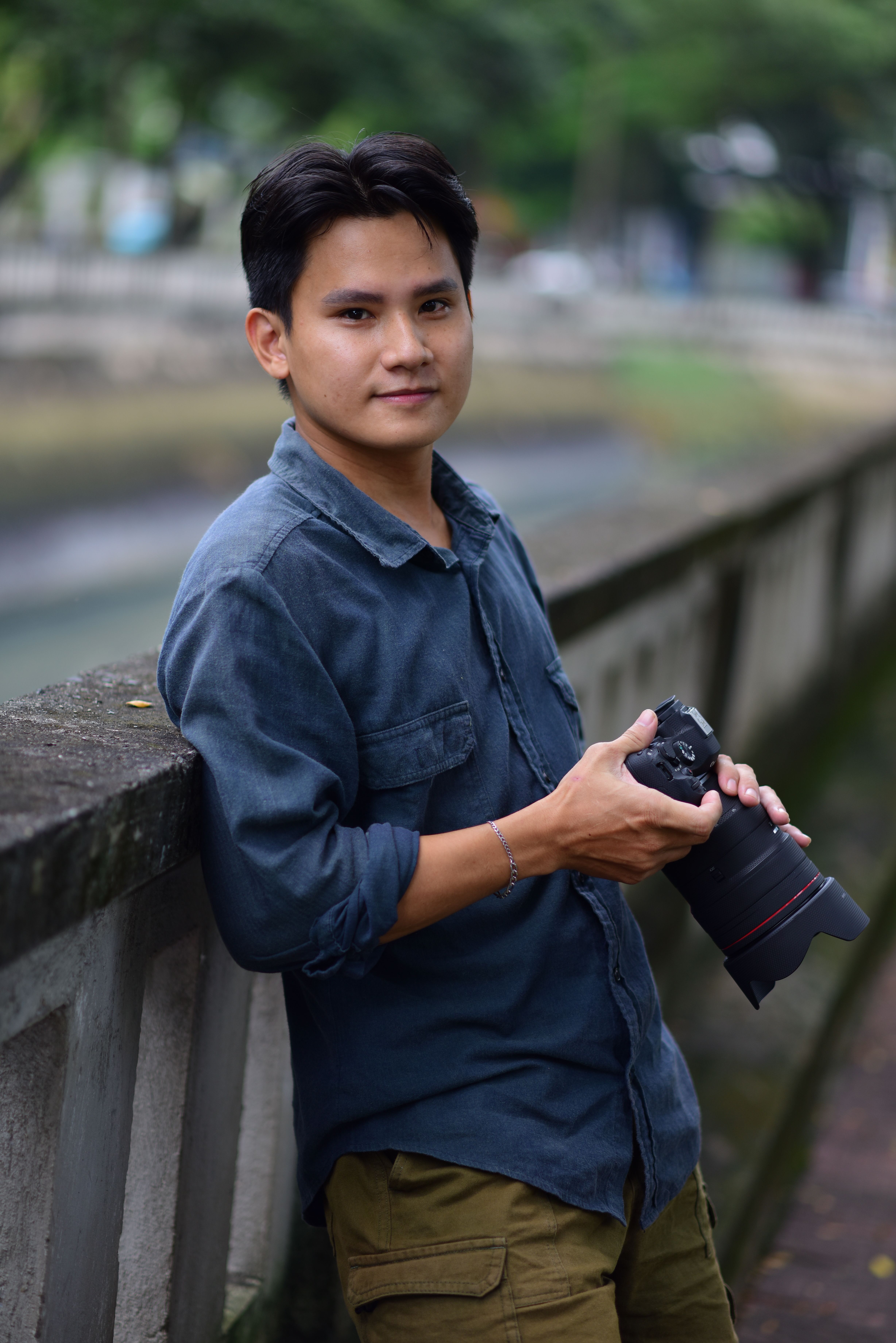Young man holding a camera, standing by a canal, showcasing outdoor photography.