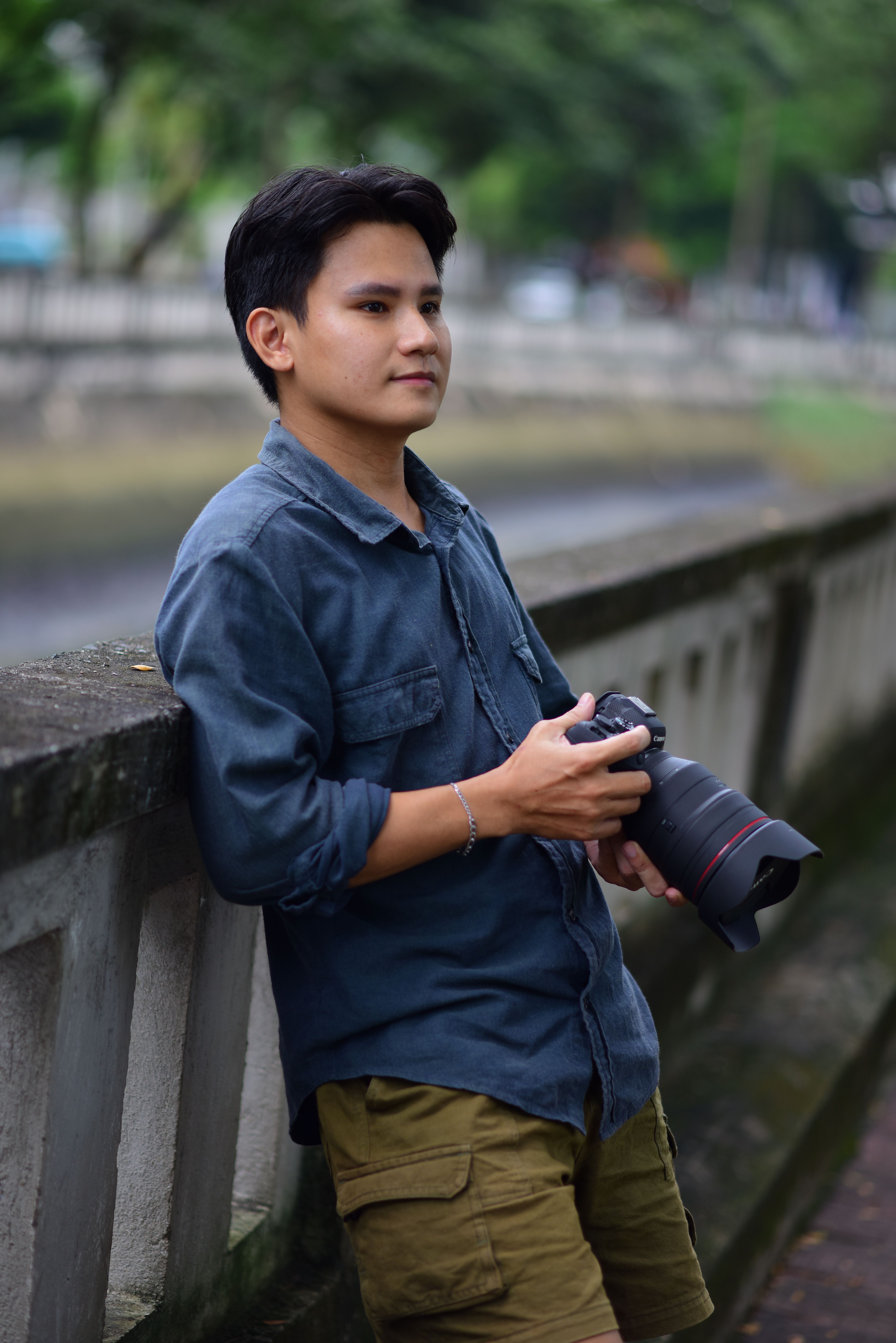 Young male photographer in casual attire holding a camera outdoors.