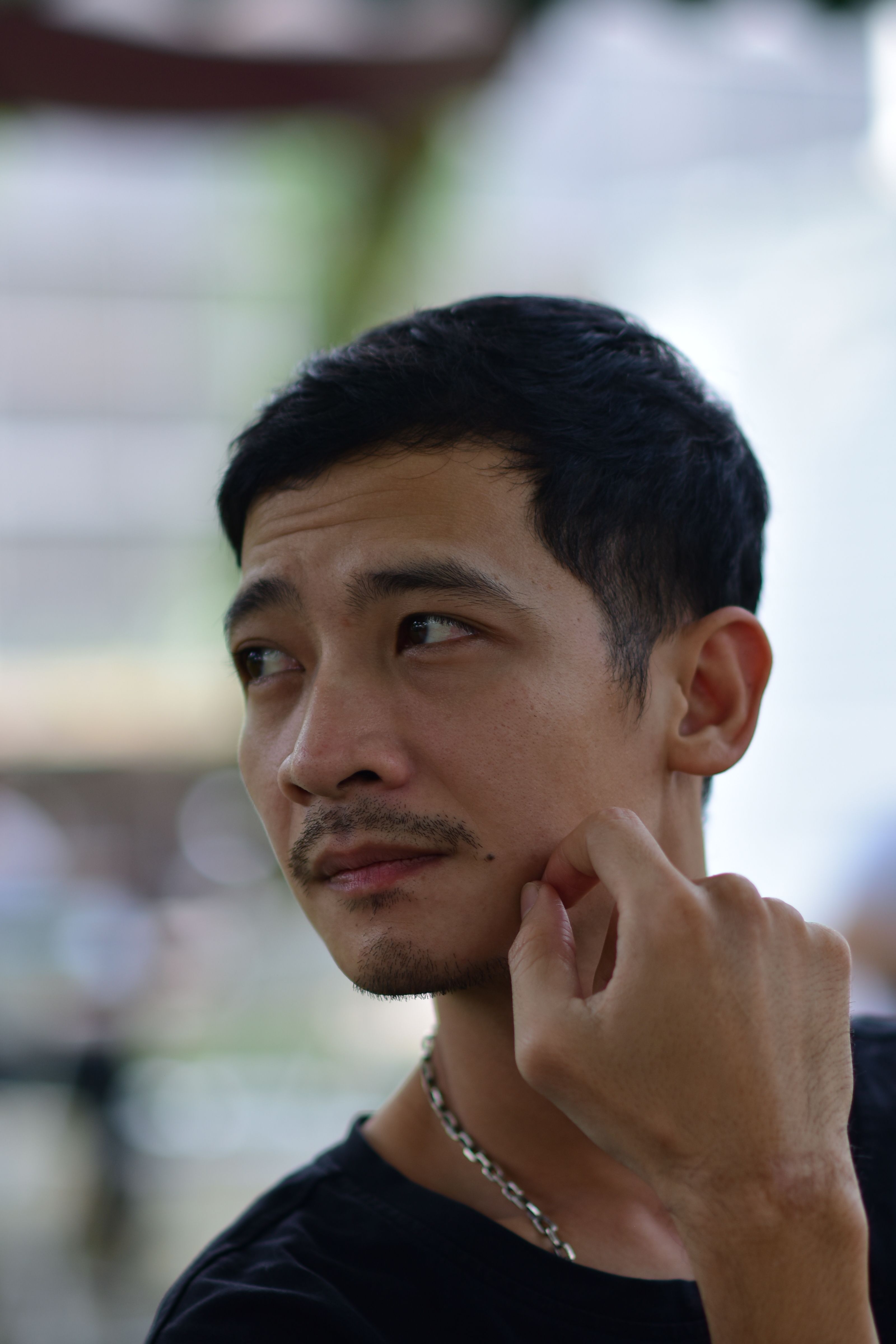 Portrait of a young man lost in thought, outdoors with blurred background.
