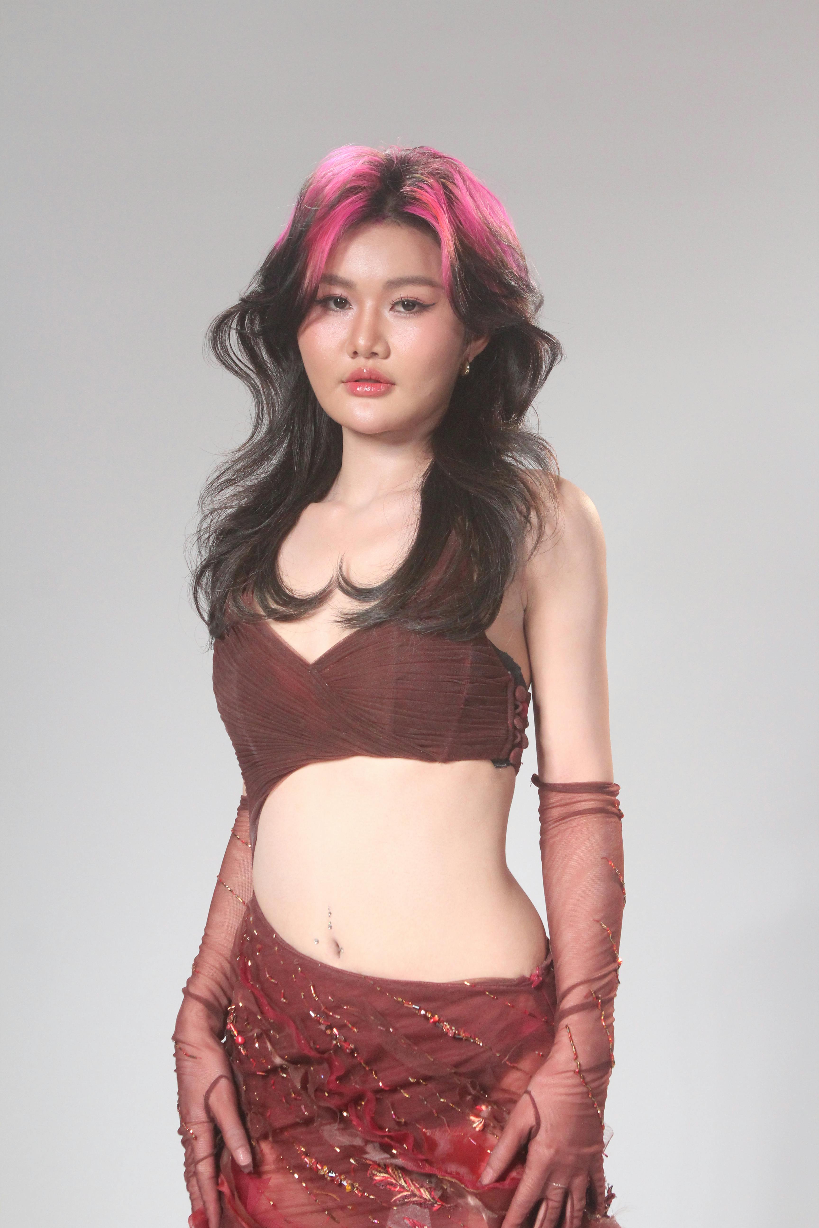 common:alt.prefix Pembe saç röfleli genç bir yetişkin, modaya uygun bir kıyafetle şık bir poz veriyor. common:alt.postfix