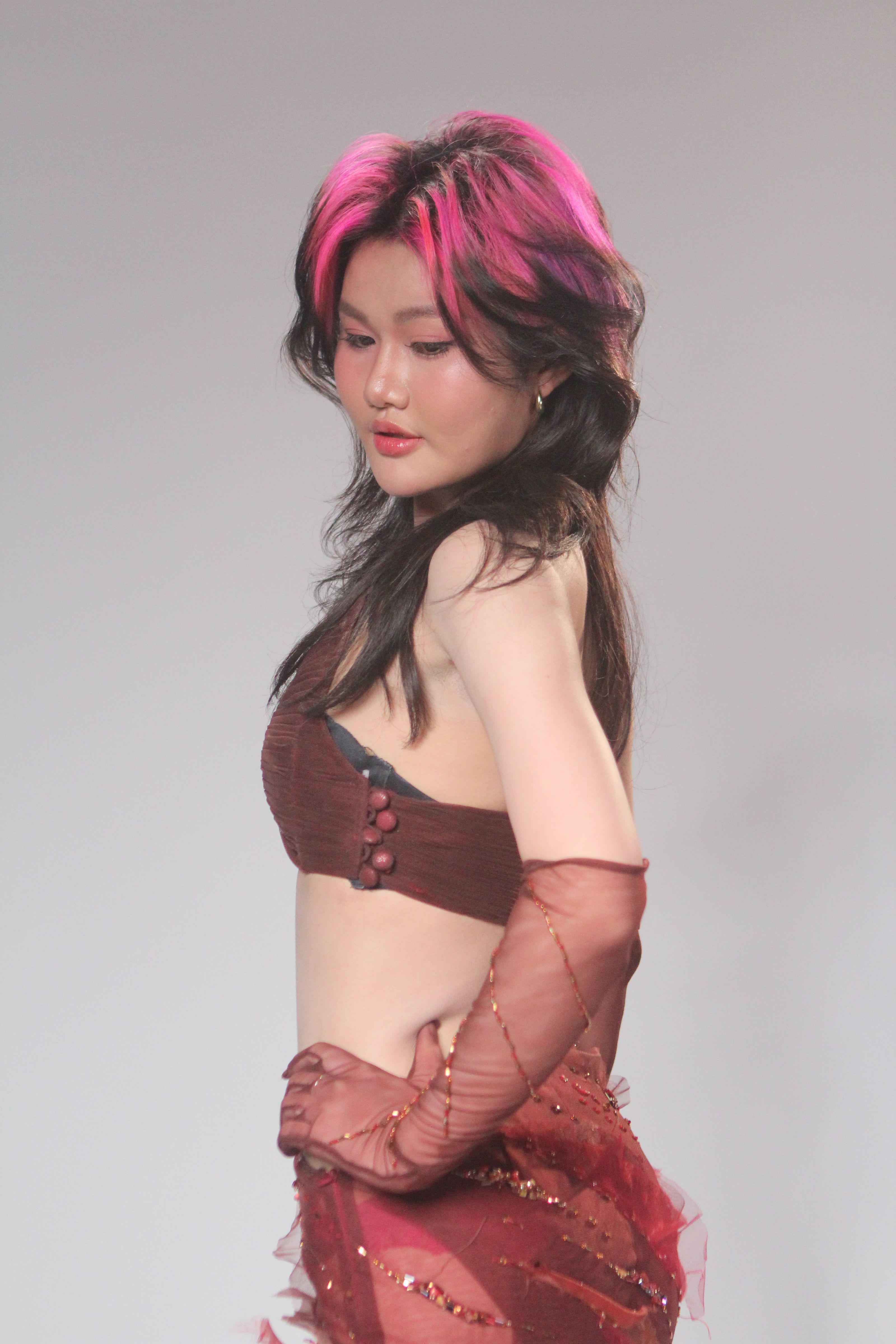 Pose impressionante de uma modelo com cabelo rosa e roupa vermelha na passarela durante um desfile de moda.