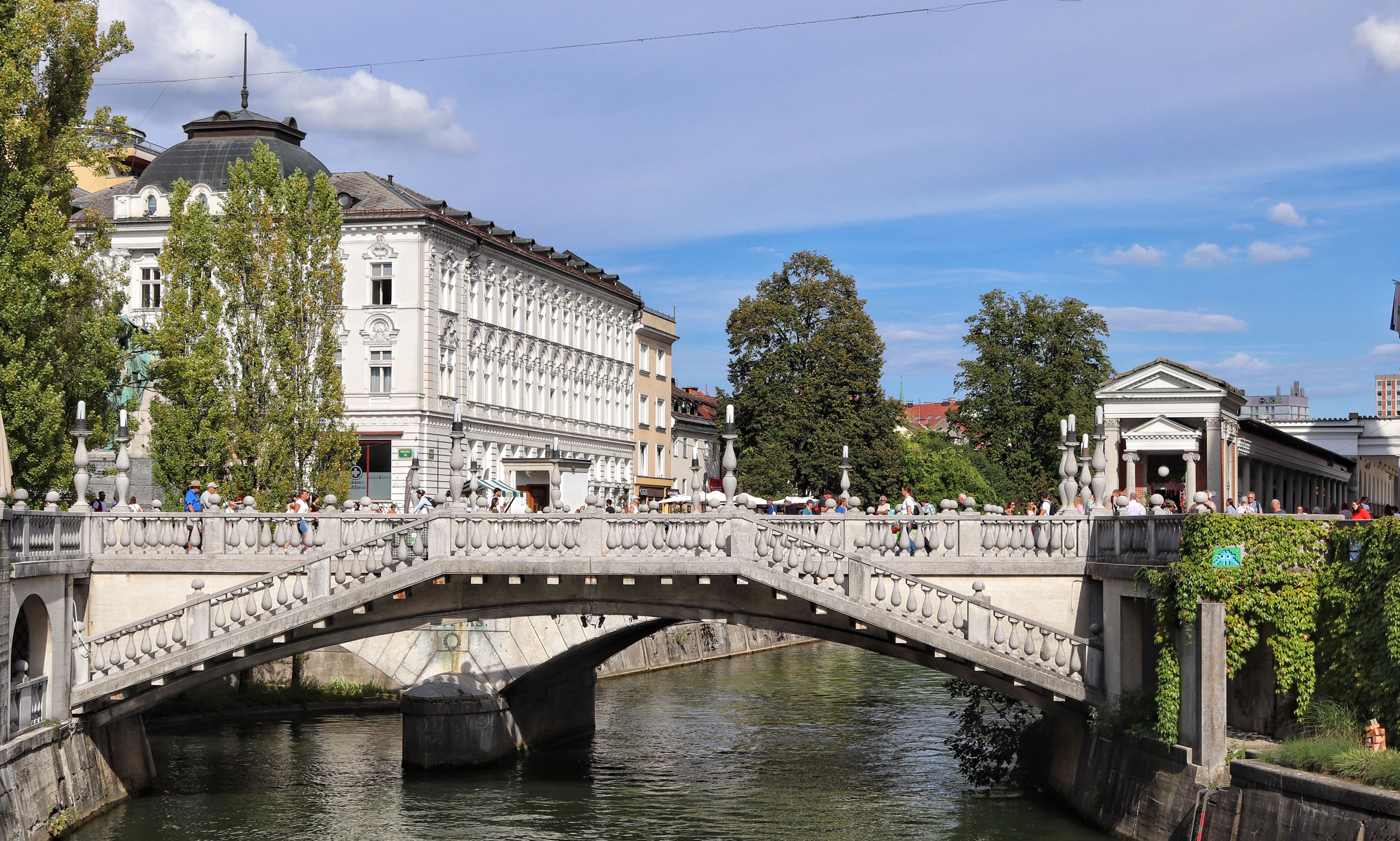 Triple Bridge in Ljubljana with pedestrians and historic buildings on a sunny day