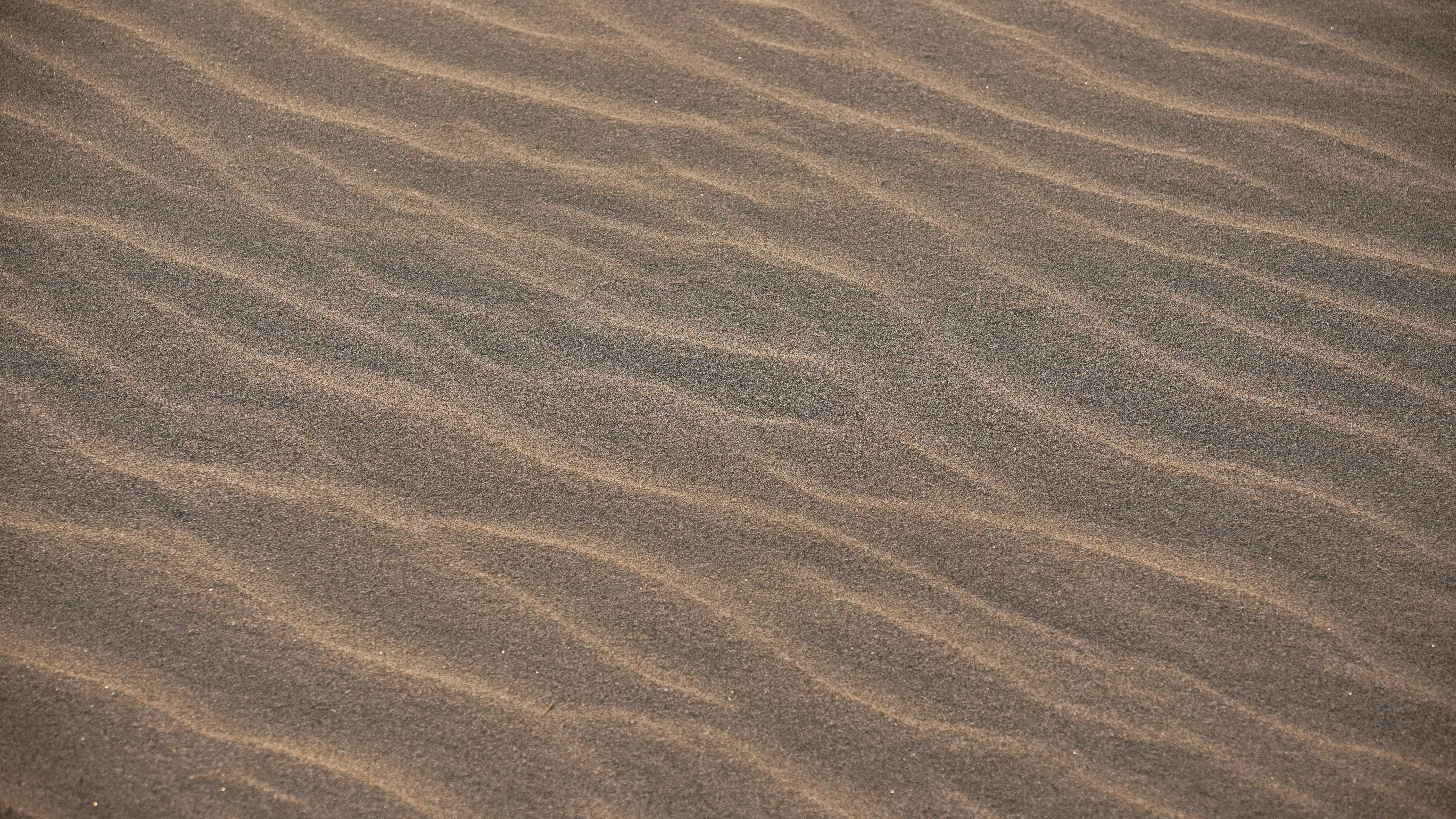 Gratuit Capture d'ondulations de sable texturées sur une plage illuminée par la chaude lumière du coucher de soleil. Photos