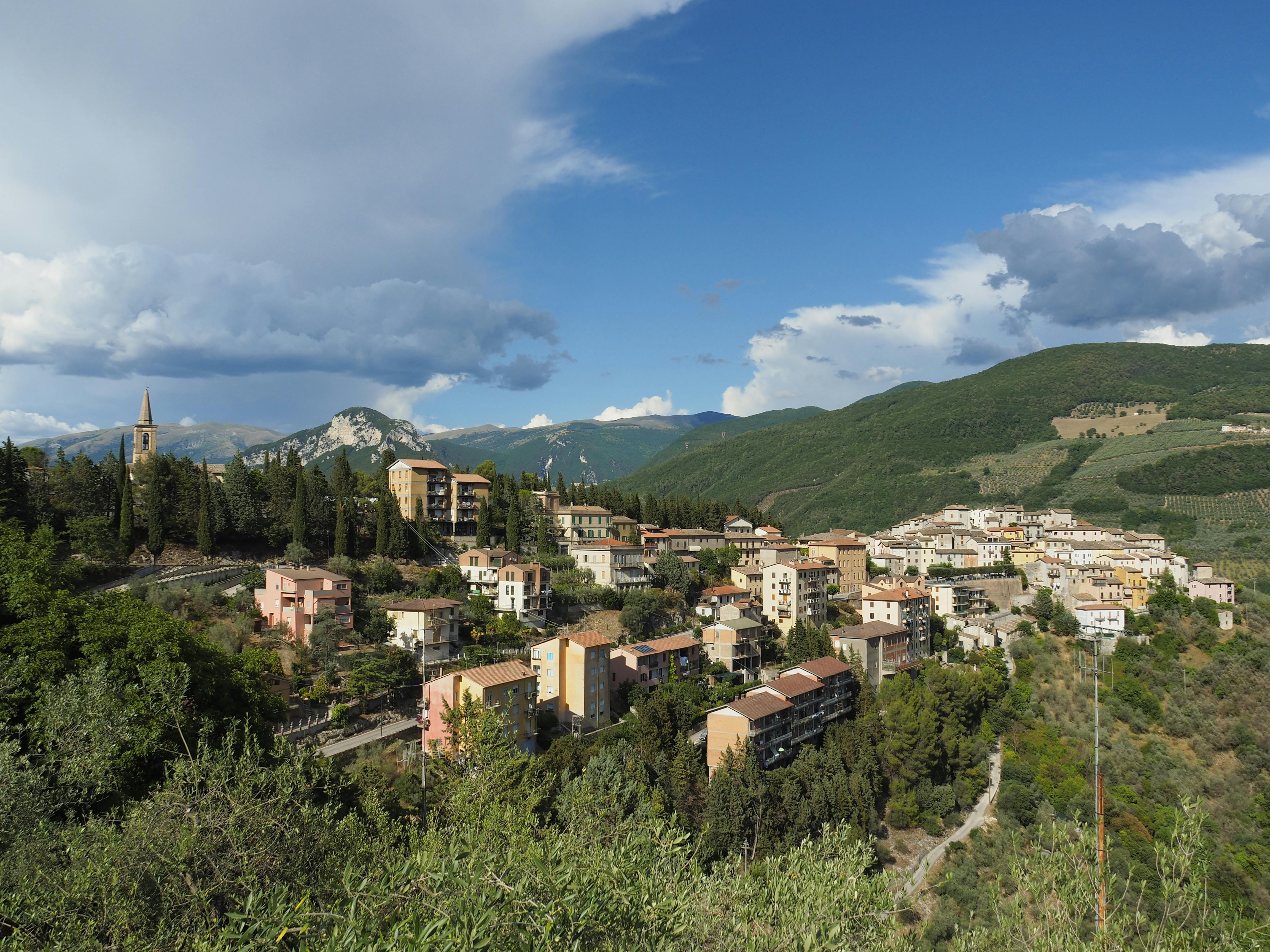 Picturesque view of an Italian hill town nestled among lush green hills under a vibrant sky.