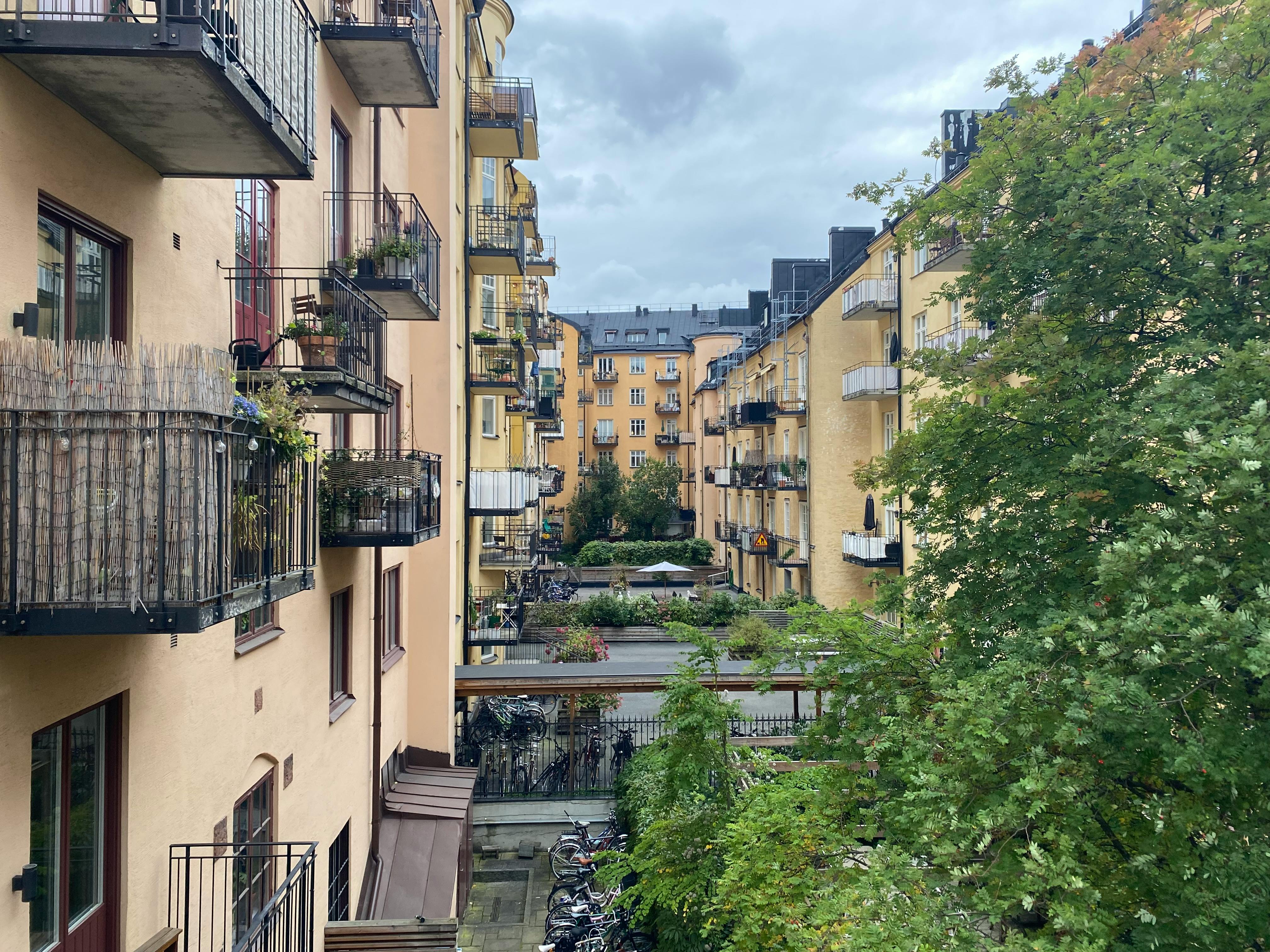 Charming urban courtyard with yellow apartments and lush greenery on a cloudy day.