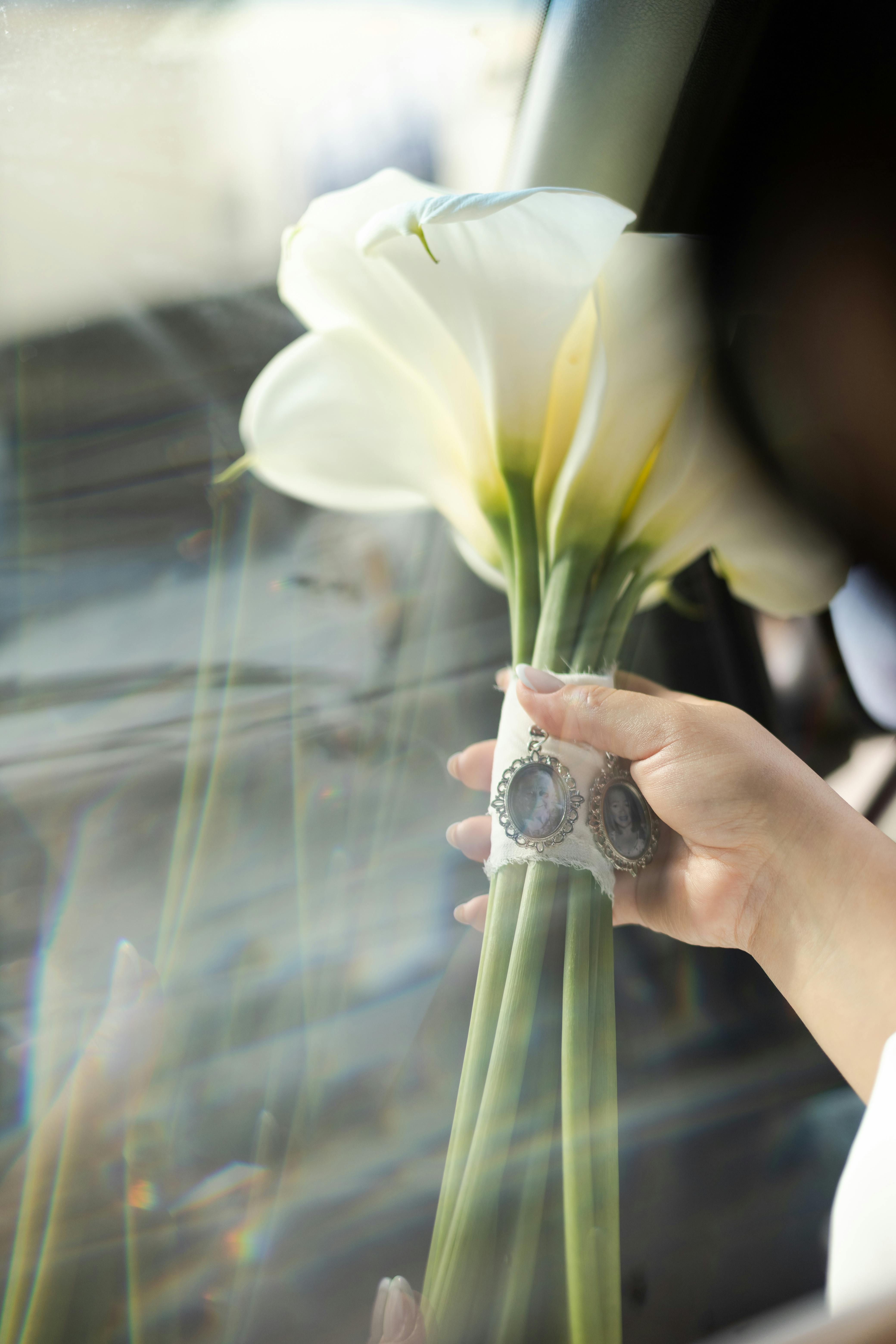 A close-up of a bridal bouquet with elegant calla lilies through a car window.