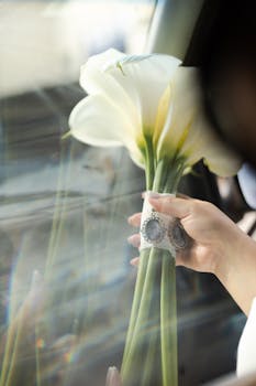 A close-up of a bridal bouquet with elegant calla lilies through a car window.