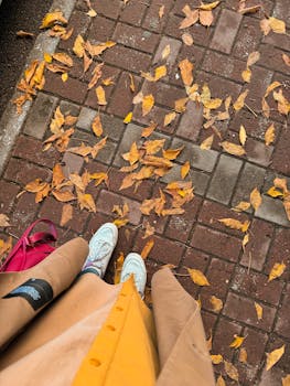 Overhead view of autumn leaves on a brick sidewalk with stylish shoes and outfit.