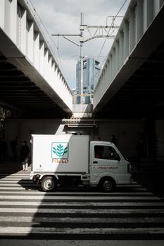Mini truck passes under railway bridge in Tokyo's Shiba district with a modern skyscraper view.