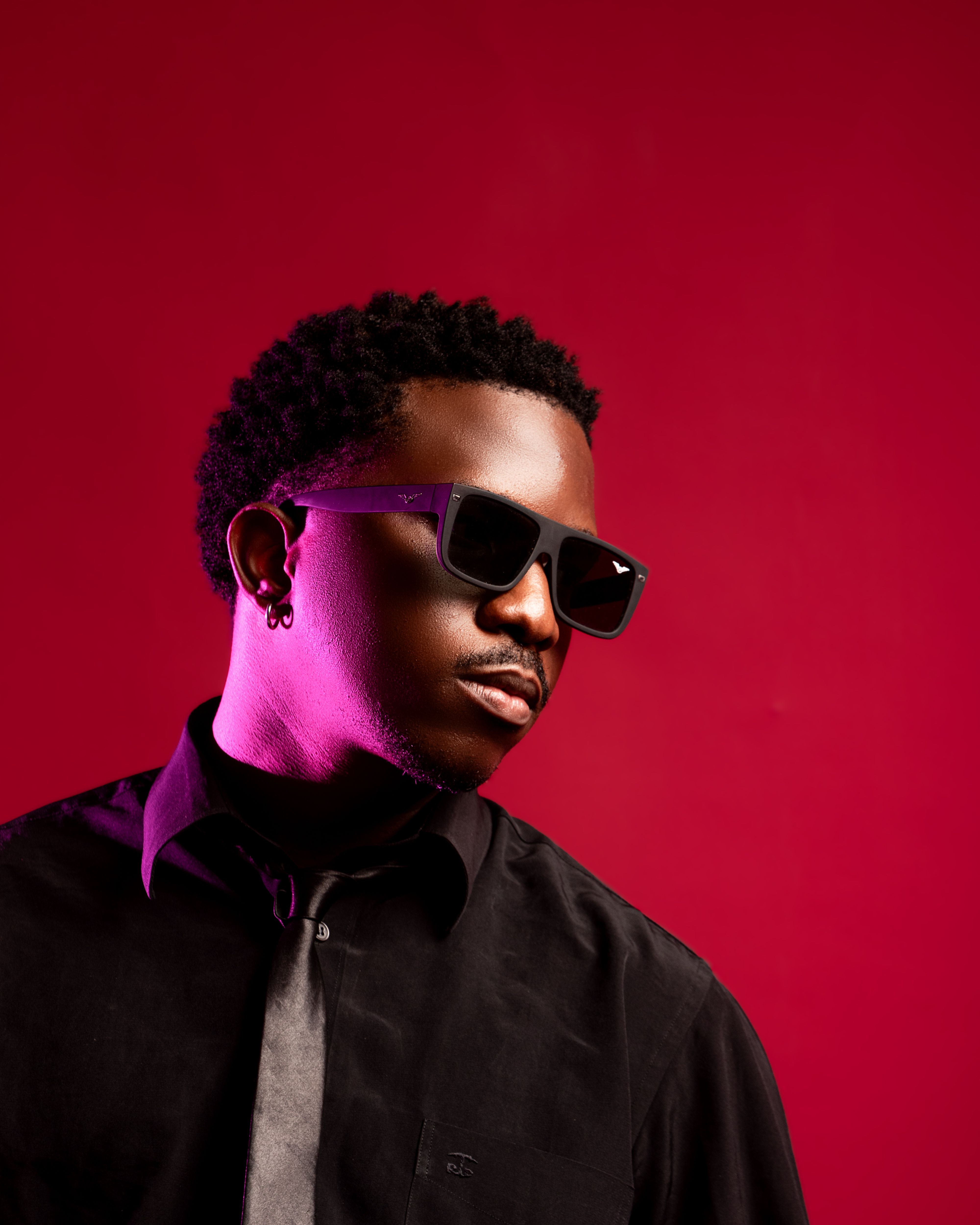 Portrait of a fashionable man wearing sunglasses and a black shirt with a vibrant red backdrop.