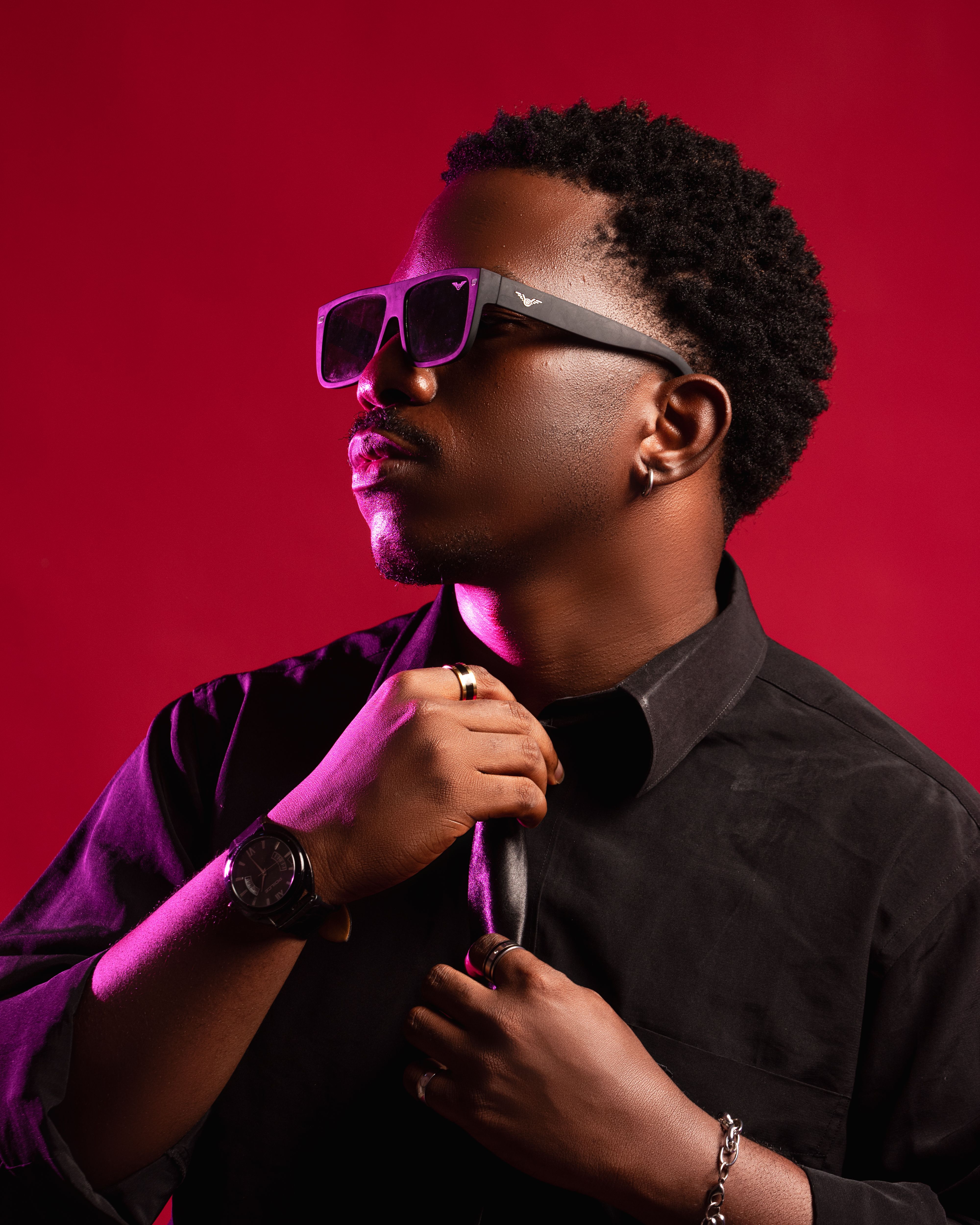 Confident man posing with sunglasses and stylish attire on red background.