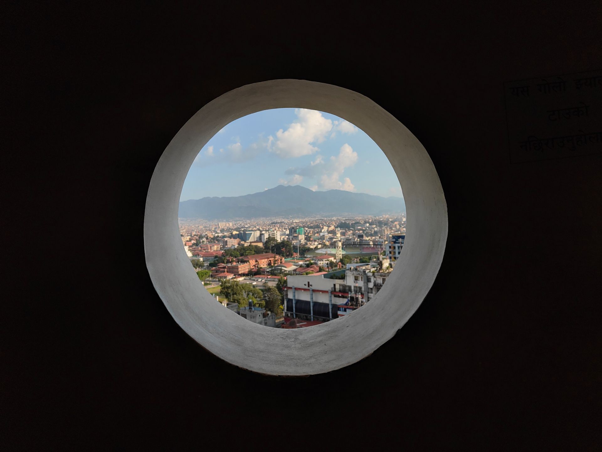 Stunning cityscape seen through a circular window with mountain backdrop.