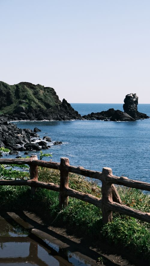 Free Experience the beautiful coastal cliffs and tranquil waters of Jeju Island's rugged shoreline, captured in stunning detail. Stock Photo