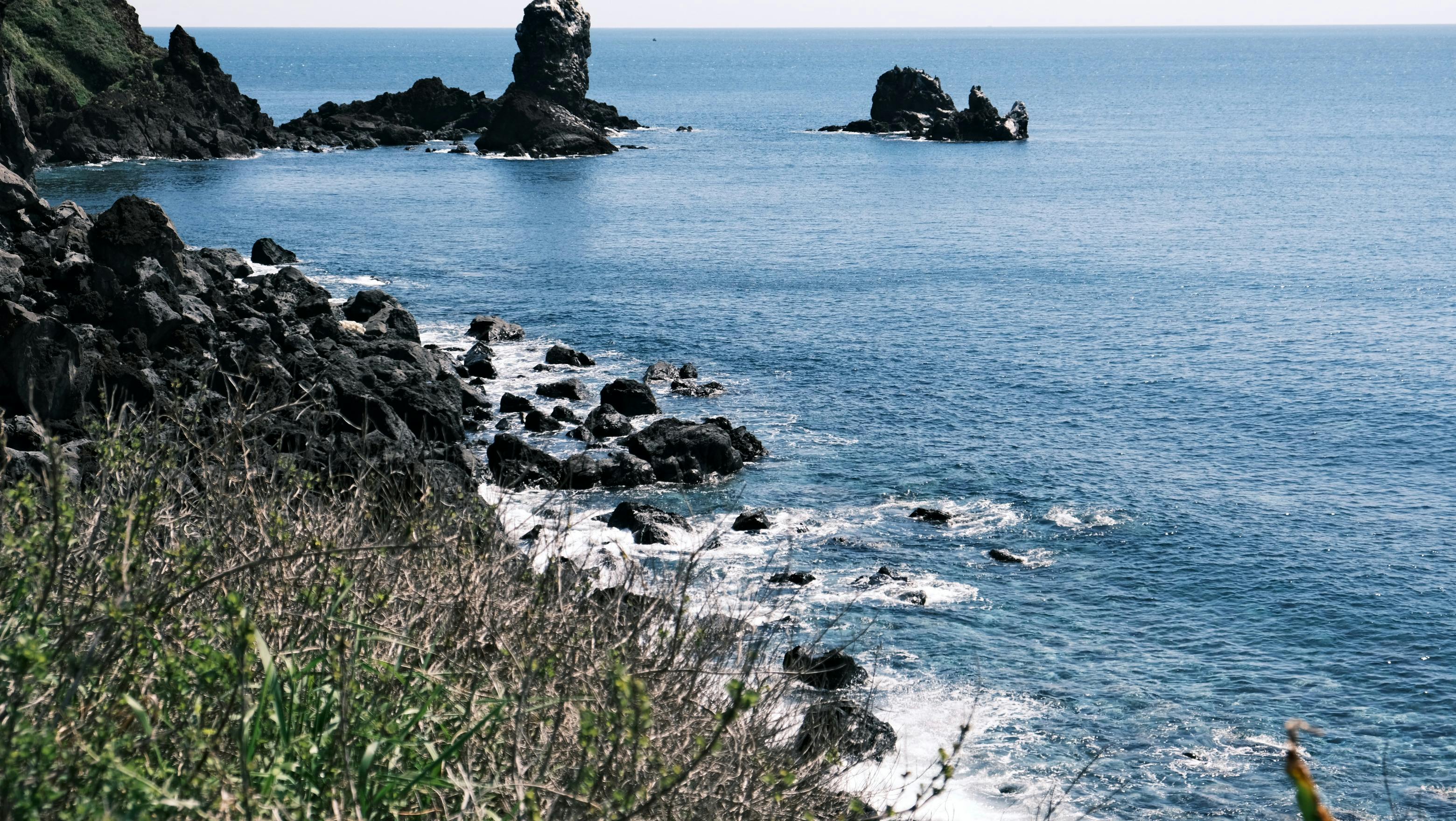 Explore the rugged beauty of Jeju Island's rocky coastline with clear blue seas and natural formations.
